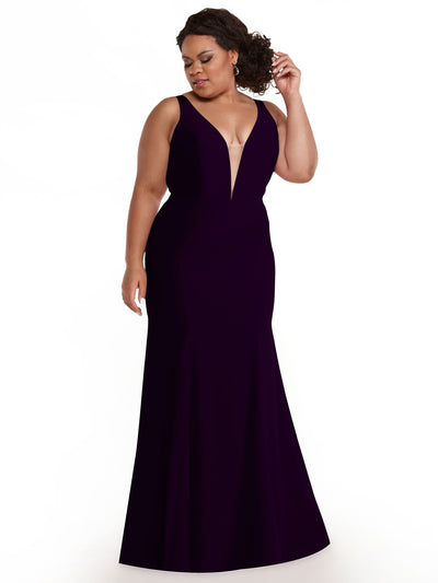 A woman models Avery Austin’s 83010 mermaid dress in eggplant, featuring a plunging V-neckline, as she stands against a white background, gently holding her curly hair back and looking down.