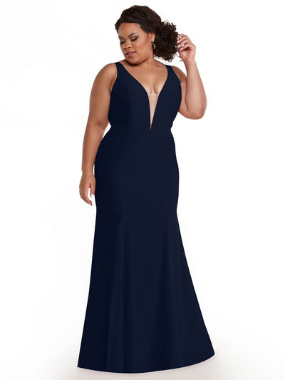 A woman in the Avery Austin 83010, a midnight sleeveless mermaid gown with a plunging neckline, stands against a white background, looking down and touching her curly hair.