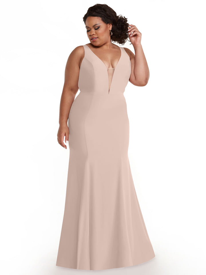 A woman in the Avery Austin 83010, a rose pink floor-length mermaid dress with a plunging neckline, stands against a white background, softly smiling as she holds her hair with one hand and looks down.