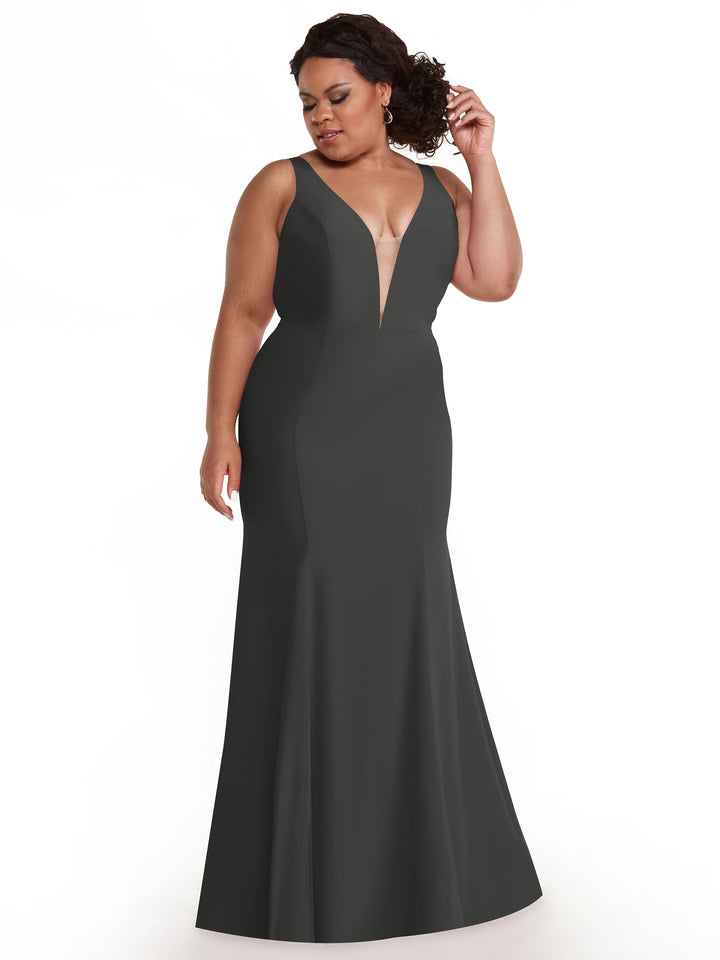 A woman in the Avery Austin 83010, a floor-length steel gray mermaid gown with a plunging neckline, stands against a white background, looking to the side and adjusting her hair.