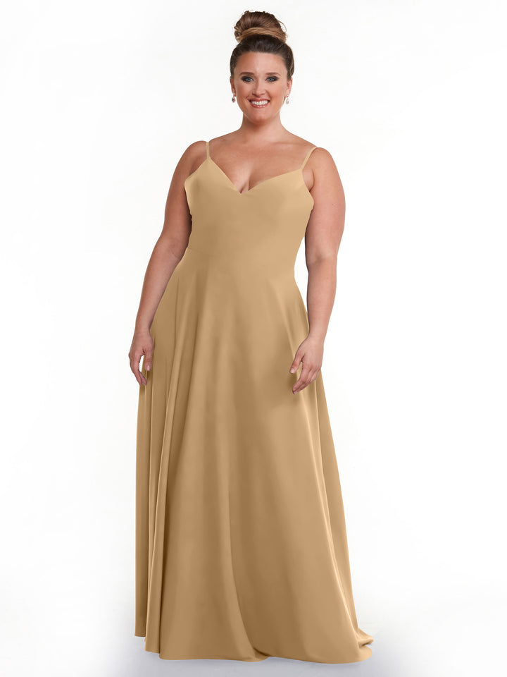 A woman with brown hair in an updo wears Avery Austin’s 83012—a long, cappuccino A-line dress with spaghetti straps and a V-neckline—standing and smiling against a plain white background.