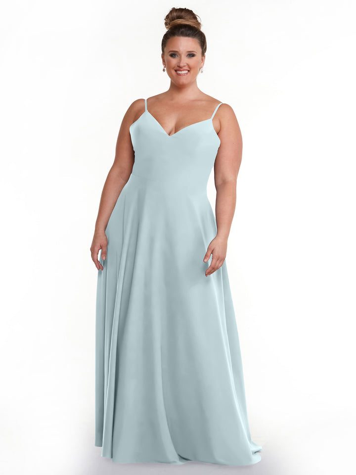 A woman with brown hair in a bun smiles while wearing Avery Austin’s 83012: a sleeveless light blue A-Line dress with spaghetti straps and a V-neckline, standing against a plain white background.