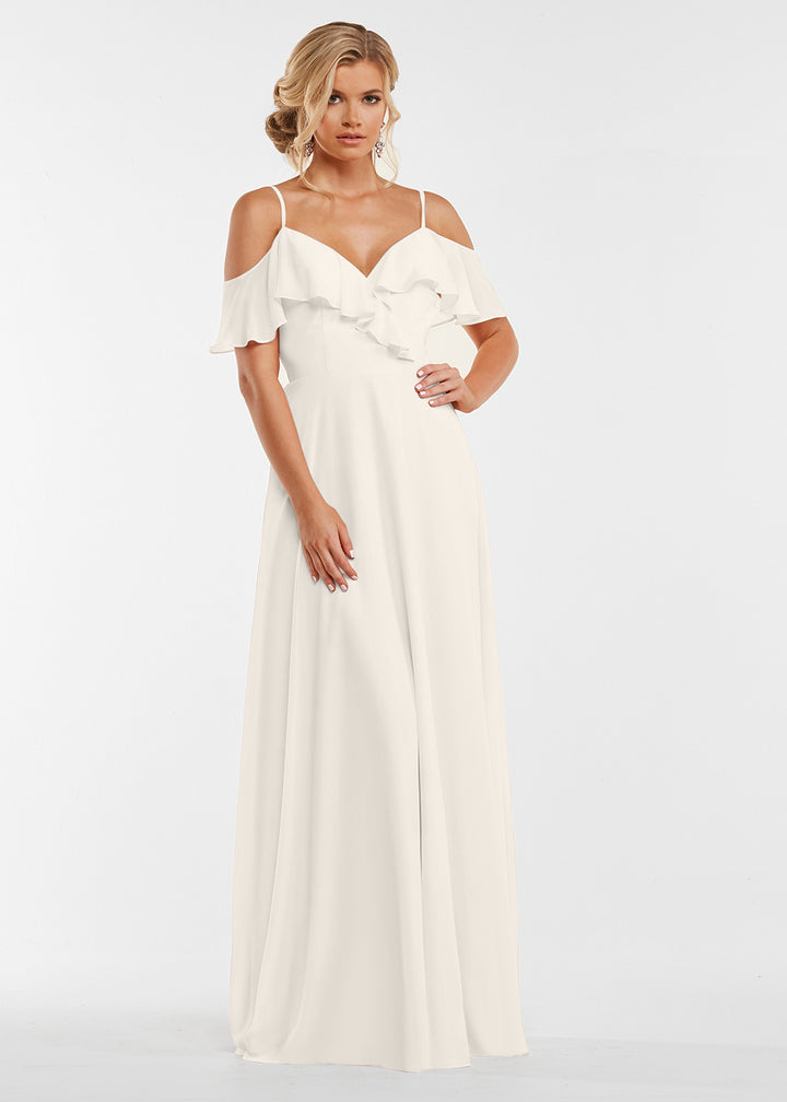 A woman models Avery Austin’s 83013—a long white dress with ruffle details and an elegant ruffled neckline—against a plain white background.