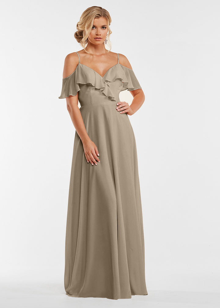 A woman wears the Avery Austin 83013 gown featuring a taupe hue, off-the-shoulder ruffled neckline, and elegant bodice details, posed against a white background.