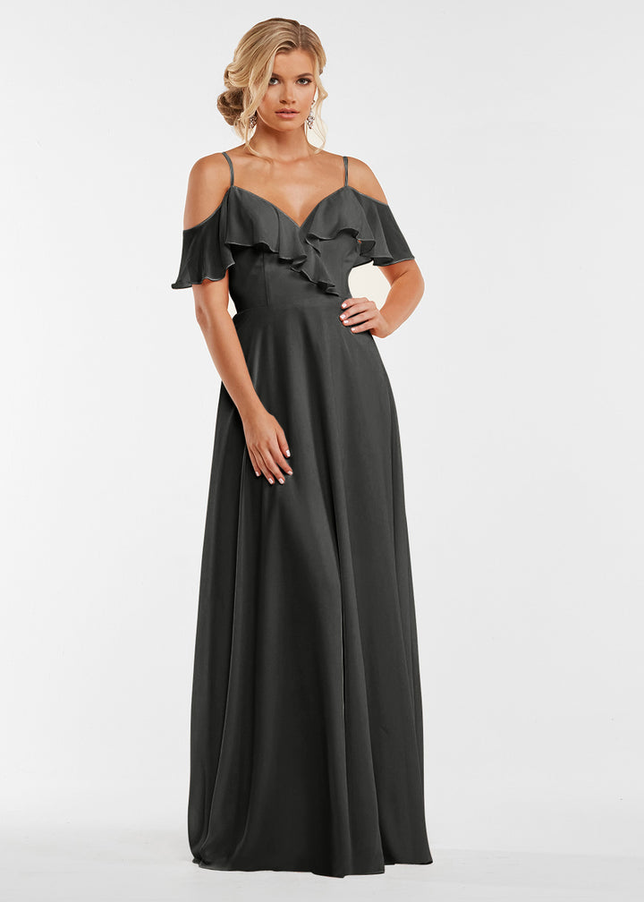A woman models Avery Austin’s 83013: a long, dark gray dress with a ruffled neckline, spaghetti straps, and a flowing skirt, set against a plain white background.