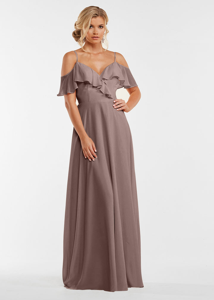 A woman models Avery Austin’s 83013: a floor-length mauve dress with off-the-shoulder sleeves, spaghetti straps, and a ruffled neckline, standing against a plain white background.