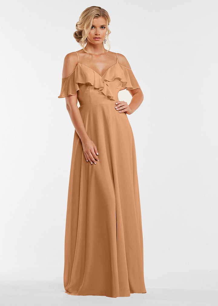 A woman models Avery Austin’s 83013, a floor-length light brown gown with an off-the-shoulder ruffled neckline and fitted bodice, standing against a plain white background.