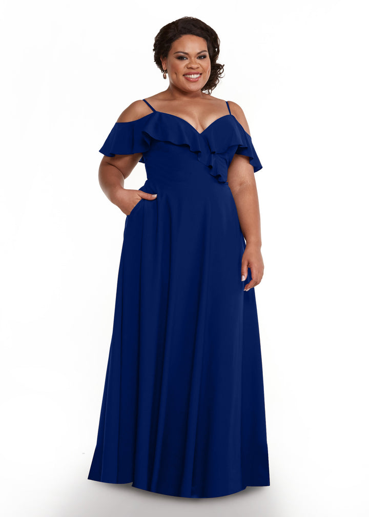 A woman poses against a white background wearing the Avery Austin 83013, a floor-length royal blue off-the-shoulder dress with ruffle details and pockets, accessorized with earrings.