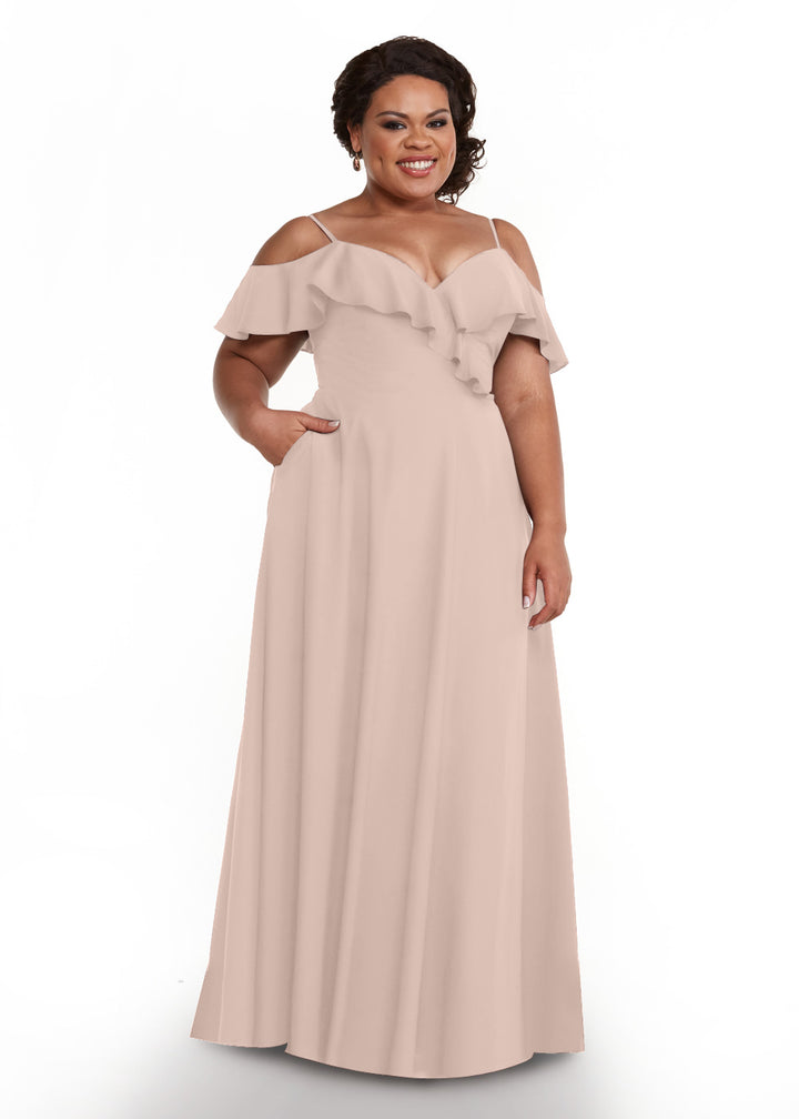 A woman smiles in the Avery Austin 83013 gown, a rose pink, floor-length dress with off-the-shoulder sleeves, spaghetti straps, ruffled neckline, and handy pockets, posing against a crisp white background.