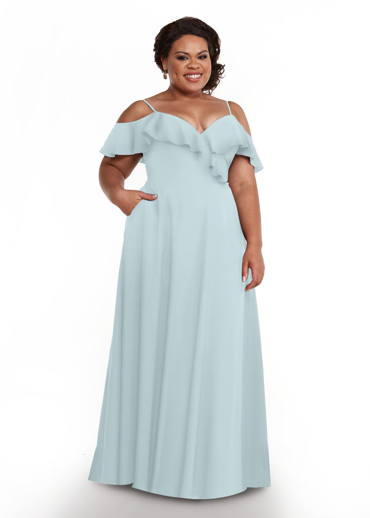 A smiling woman models Avery Austin 83013, a light blue, floor-length dress with off-the-shoulder sleeves, ruffled neckline, and delicate spaghetti straps, against a plain white background.