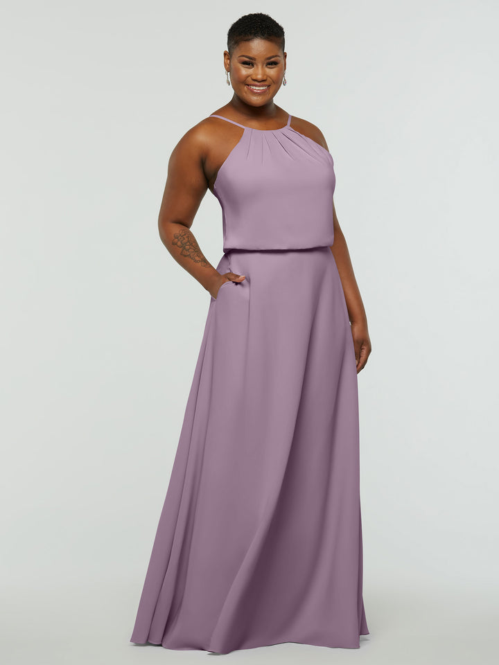 A smiling person wears Avery Austin’s 83015—a sleeveless, floor-length lavender A-line halter dress with pockets—standing against a plain light background.