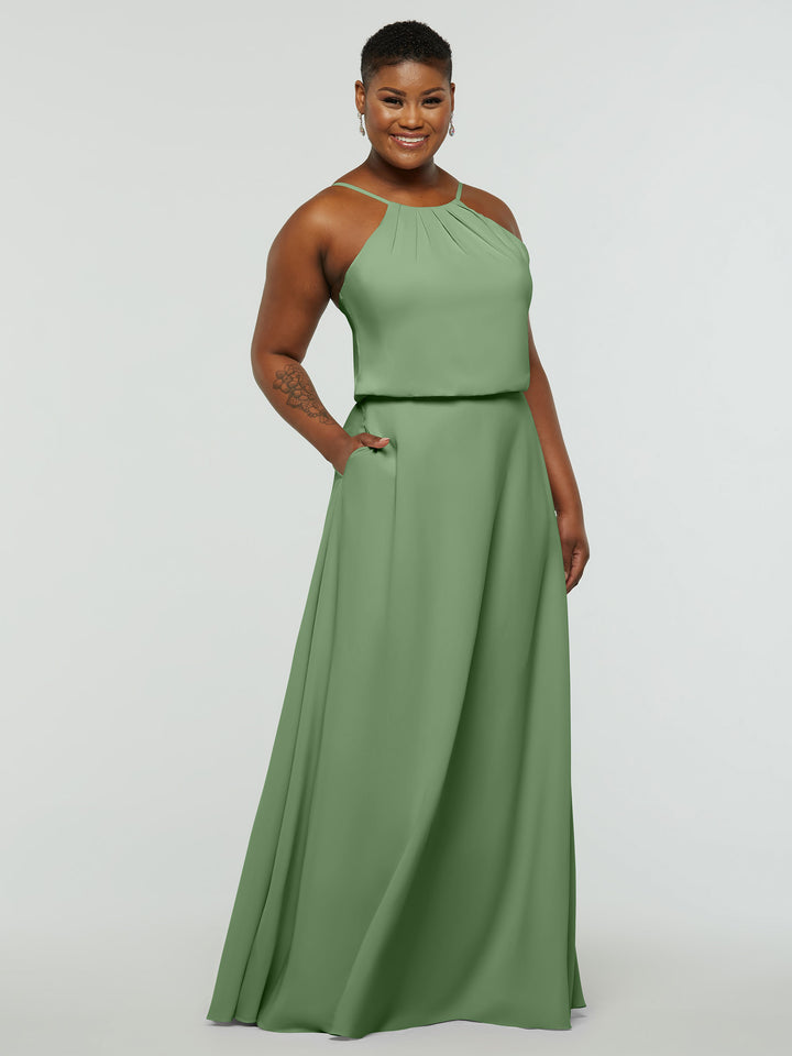 A person smiles in the Avery Austin 83015, a sleeveless sage green A-line dress with a high neckline, subtle pleats, and pockets, standing against a plain light background.