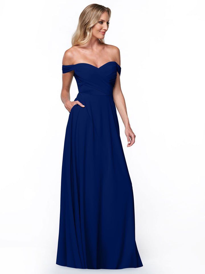 A woman models the Avery Austin 83018: a floor-length, off-the-shoulder dress with pockets, royal blue fitted bodice, and flowing A-Line skirt, standing against a plain white background.