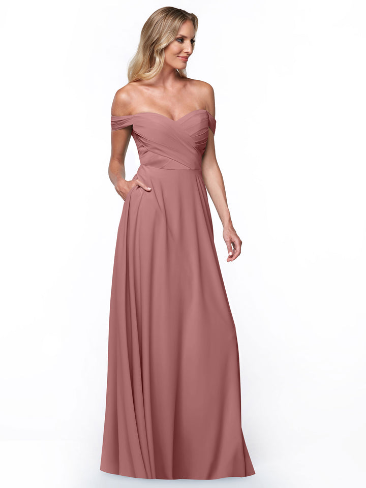 A woman models Avery Austin dress 83018, featuring a long off-the-shoulder design with a fitted ruched bodice and flowing A-line skirt, set against a plain white background.