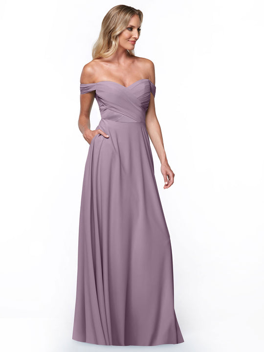 A woman in Avery Austin’s 83018, a floor-length lavender off-the-shoulder dress with pockets, pleated bodice, and elegant A-line skirt, stands against a plain white background.