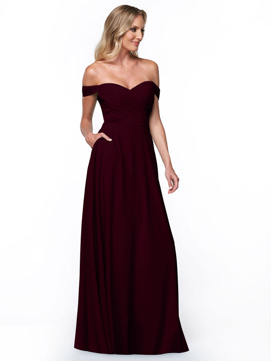 A model poses against a plain white background wearing Avery Austin’s 83018: an off-the-shoulder, dark burgundy dress featuring a fitted bodice and a flowing A-line skirt.