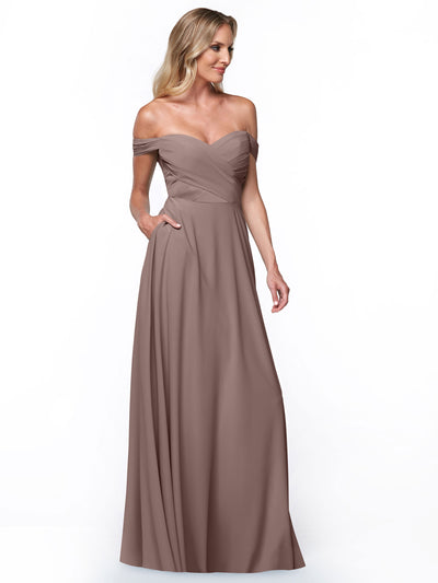 A woman models Avery Austin style 83018, a mauve off-the-shoulder dress featuring a fitted pleated bodice and flowing A-line skirt, standing against a plain white background.