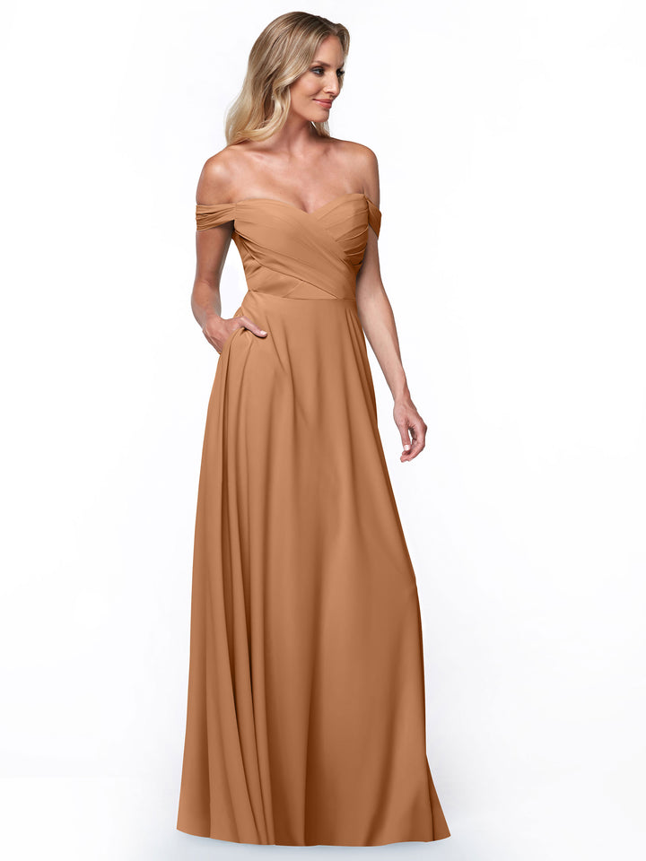 A woman wearing Avery Austin’s 83018, a light brown off-the-shoulder dress with an A-line skirt and fitted bodice, poses against a plain white background.