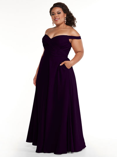 A woman models Avery Austin style 83018: an off-the-shoulder deep purple dress with pockets, a fitted bodice, and a flared A-line skirt. She poses confidently with one hand in her pocket against a white background.