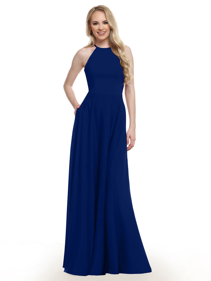 A woman with long blonde hair wears the Avery Austin 83022, a sleeveless, floor-length royal blue A-line gown, and smiles with one hand in her pocket against a plain white background.