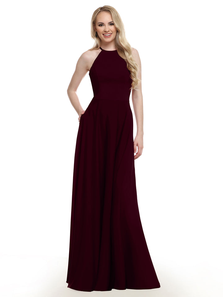 A smiling woman with long blonde hair models Avery Austin’s 83022, a sleeveless burgundy A-line gown with a fitted bodice and floor-length skirt, standing before a plain white backdrop.