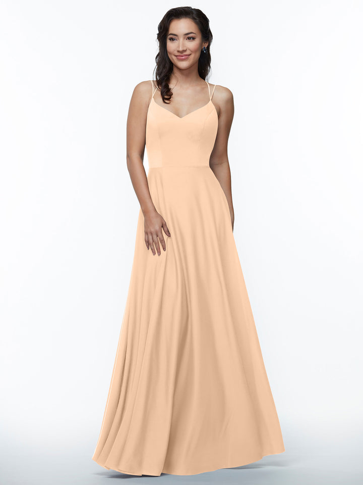 A woman with wavy dark hair smiles as she wears Avery Austin’s 83024, an elegant peach A-line dress with double spaghetti straps and a flowing skirt, set against a white background.