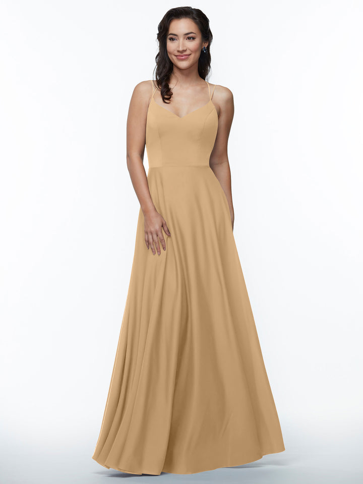 A woman in the Avery Austin TH-83024 dress, a cappuccino A-line with double spaghetti straps, stands against a white background, smiling softly with one hand by her side and the other touching her skirt.