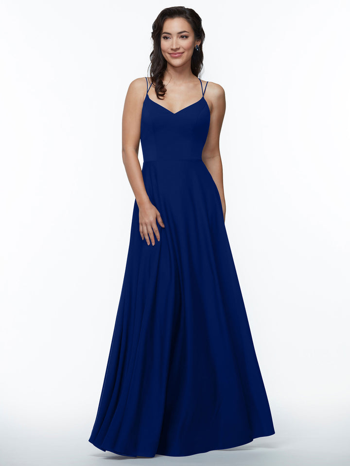 A woman with wavy dark hair smiles softly, standing against a white background in Avery Austin’s 83024—a sleeveless, royal blue A-Line dress featuring double spaghetti straps and a fitted bodice.