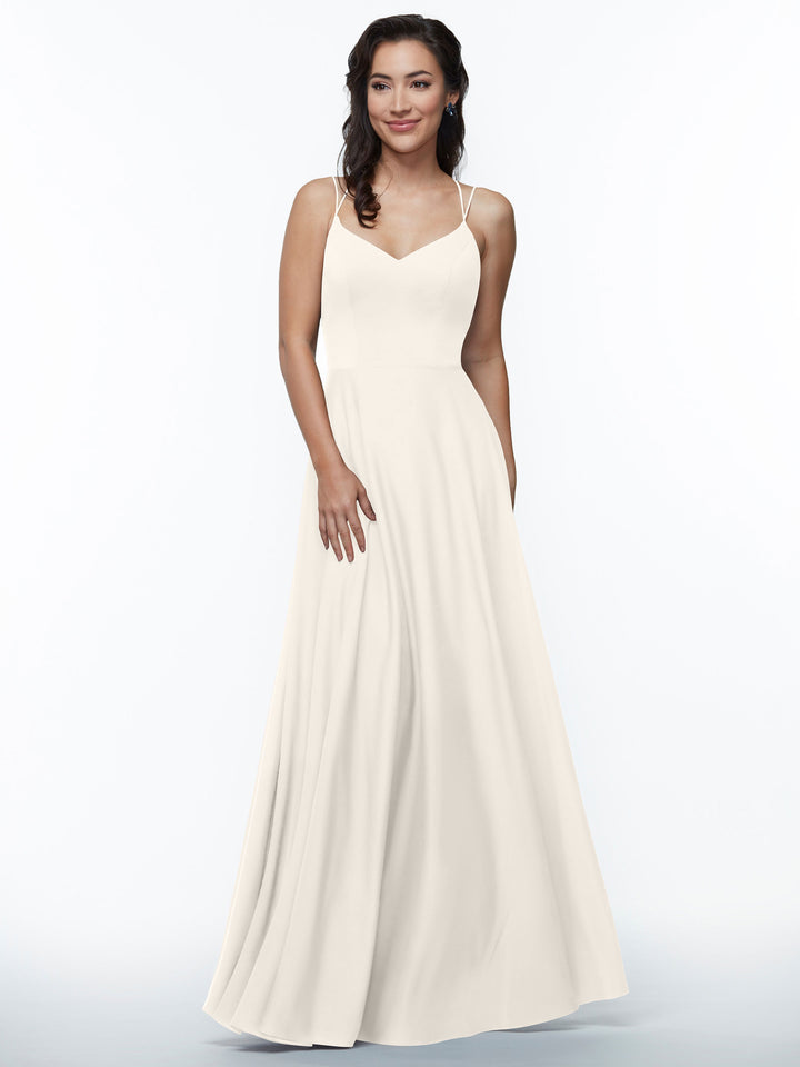 A woman with wavy dark hair models Avery Austin’s 83024, an elegant A-line dress with double spaghetti straps, standing against a plain white background and smiling gently.
