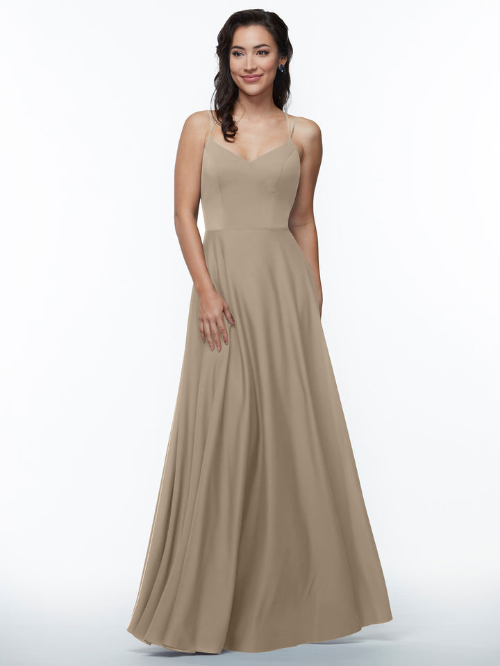 A woman with wavy dark hair stands against a white background, smiling softly and wearing Avery Austin’s 83024—a sleeveless A-line dress featuring double spaghetti straps and a fitted bodice. One hand rests by her side.