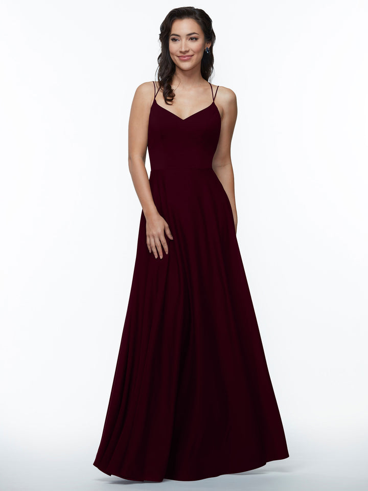 A woman with wavy dark hair smiles softly, posing against a white background in the Avery Austin TH-83024 dress—a maroon, floor-length A-Line gown with double spaghetti straps and a flared skirt.