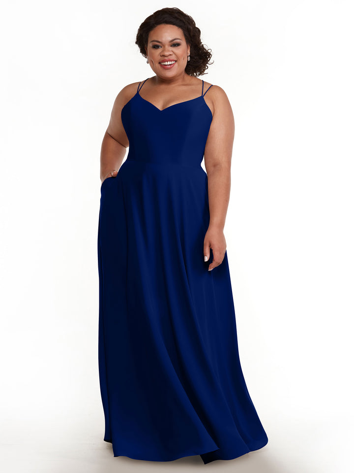 A woman wearing Avery Austin’s 83024, an elegant floor-length royal blue A-line dress with double spaghetti straps, stands smiling against a plain white background.
