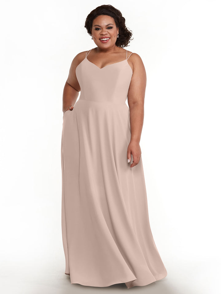 A woman in the Avery Austin 83024 A-Line dress in rose pink with double spaghetti straps stands against a white background, smiling with one hand in her pocket.