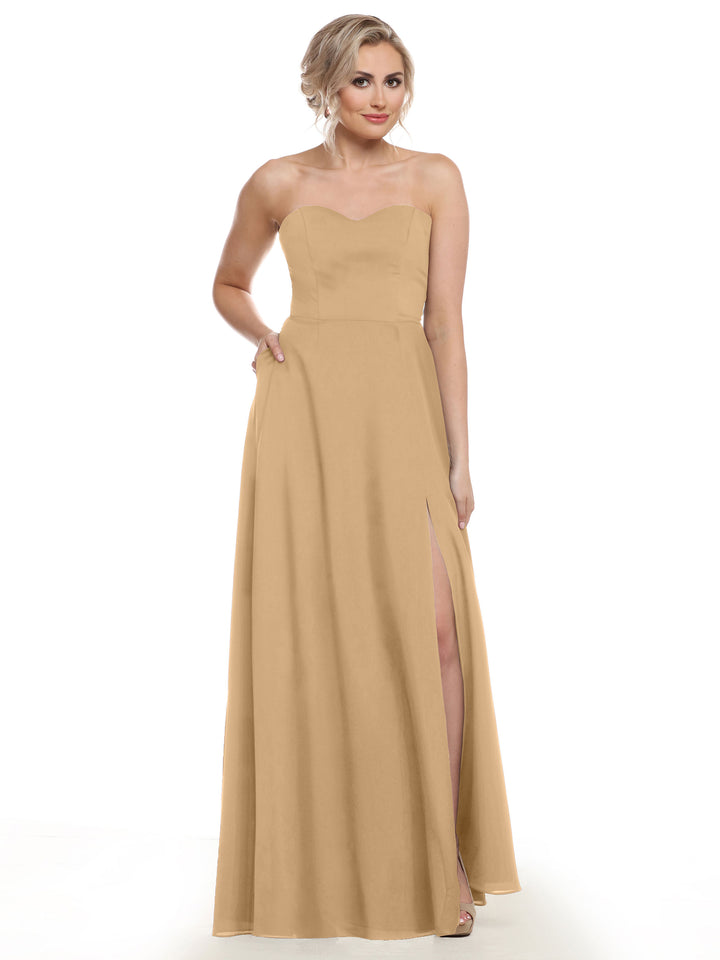 A woman stands against a white background wearing Avery Austin style 83025, a floor-length, beige, strapless bridesmaid dress featuring a sweetheart neckline and high slit.