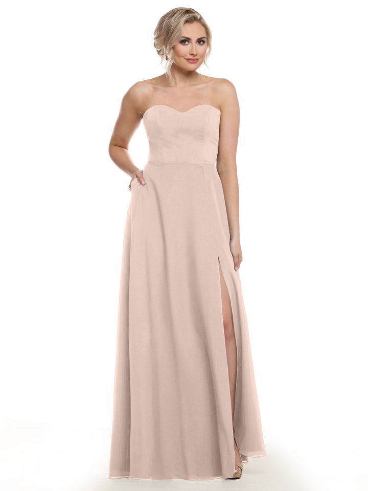 A woman stands against a plain white background wearing Avery Austin style 83025, a strapless rose pink chiffon bridesmaid dress with a sweetheart neckline, thigh-high slit, and floor-length A-line silhouette.