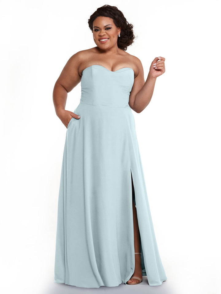 A woman smiles and raises one hand while wearing Avery Austin’s 83025—a light blue, strapless A-line bridesmaid dress with a sweetheart neckline and thigh-high slit.