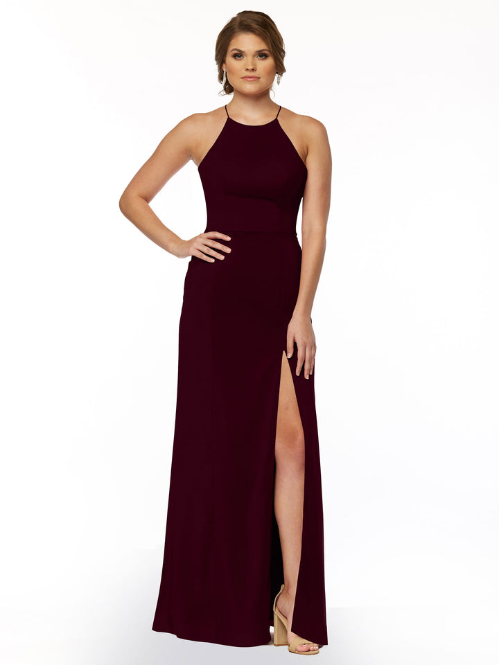 A woman stands against a white background in Avery Austin 83026, a sleeveless, floor-length burgundy sheath dress with a high neckline and thigh-high slit, styled with high heel sandals and one hand on her hip.