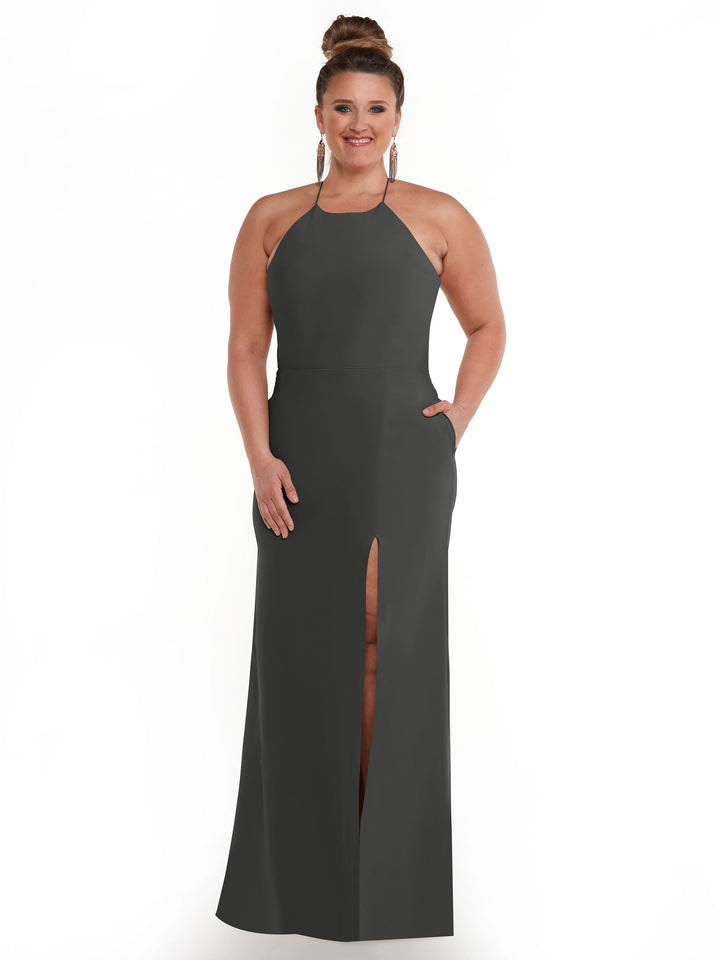 A woman with her hair in a bun wears Avery Austin’s 83026, a sleeveless, floor-length halter neck dress with a front slit and subtle pockets, smiling as she stands against a plain white background.