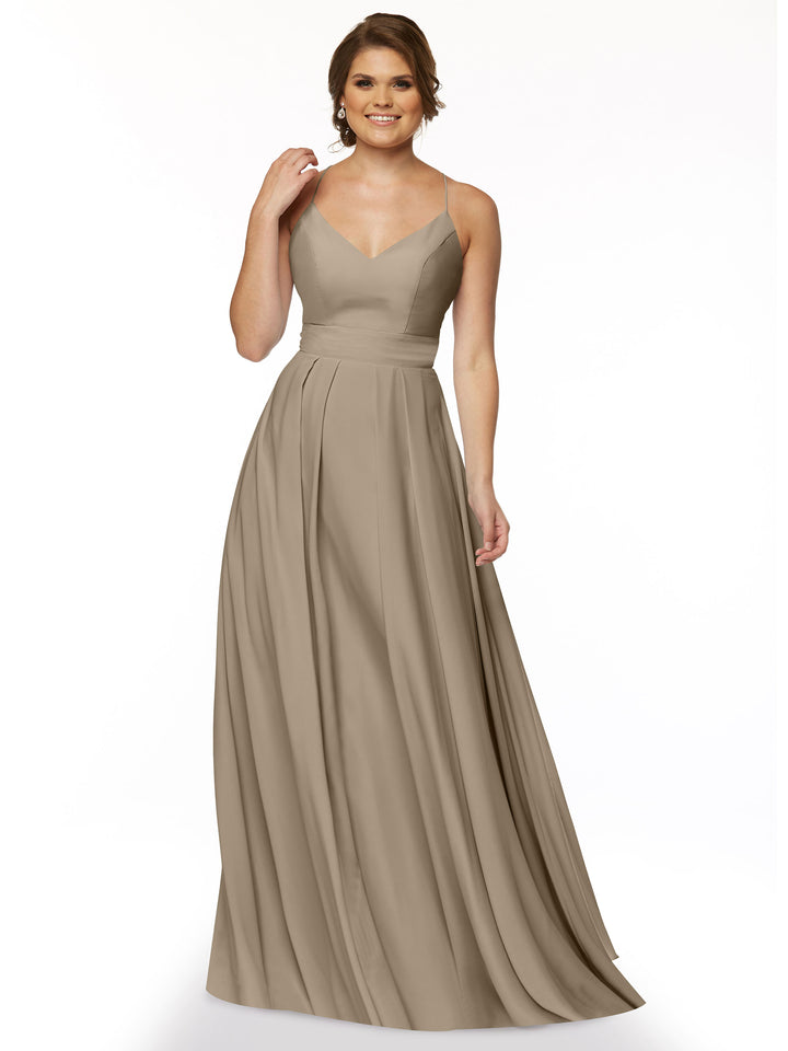 A woman stands and smiles against a plain white background, wearing Avery Austin’s 83027—a sleeveless, floor-length taupe A-line dress with a V-neckline and spaghetti straps.