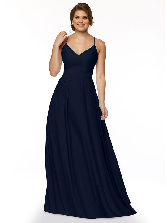 A woman in the Avery Austin 83027, a sleeveless floor-length navy A-line dress with spaghetti straps and a V-neckline, stands against a white background, smiling gently with one hand touching her hair.