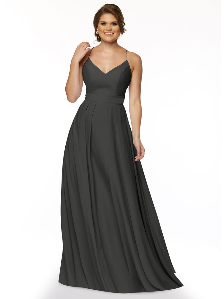 A woman in the Avery Austin 83027, a long dark gray A-line dress with spaghetti straps and a V-neckline, stands smiling against a plain white background, with one hand touching her hair.