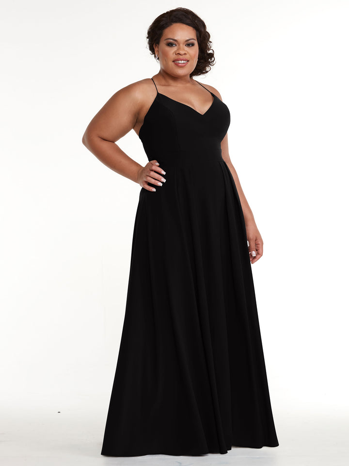 A woman smiles and poses with one hand on her hip, wearing Avery Austin style 83027—a long black A-line dress with spaghetti straps—against a white background.