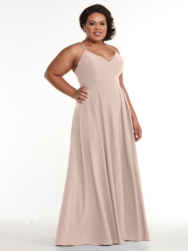 A woman in the Avery Austin 83027 dress poses against a white background, wearing a rose pink A-line gown with a fitted bodice, flowing skirt, spaghetti straps, and V-neck; she smiles with styled dark hair.