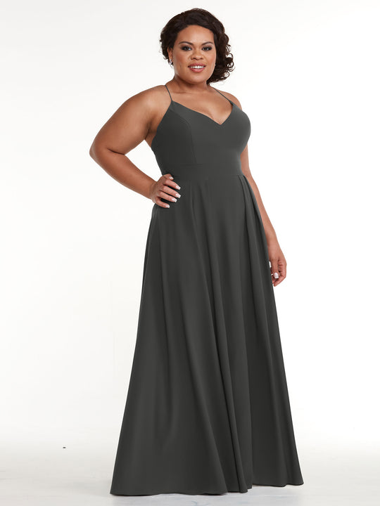 A woman models the Avery Austin TH-83027, a long, sleeveless dark gray A-line dress with a V-neckline, smiling with one hand on her hip against a plain white background.