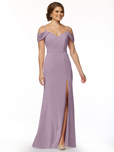 A woman stands and smiles against a plain white background, wearing Avery Austin’s 83029—a floor-length, lavender off-the-shoulder dress with draped sleeves and a thigh-high slit.