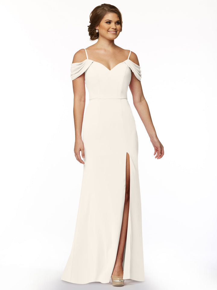 A woman models Avery Austin’s 83029: a long, off-the-shoulder dress with draped sleeves and a thigh-high slit, posed against a plain white background.
