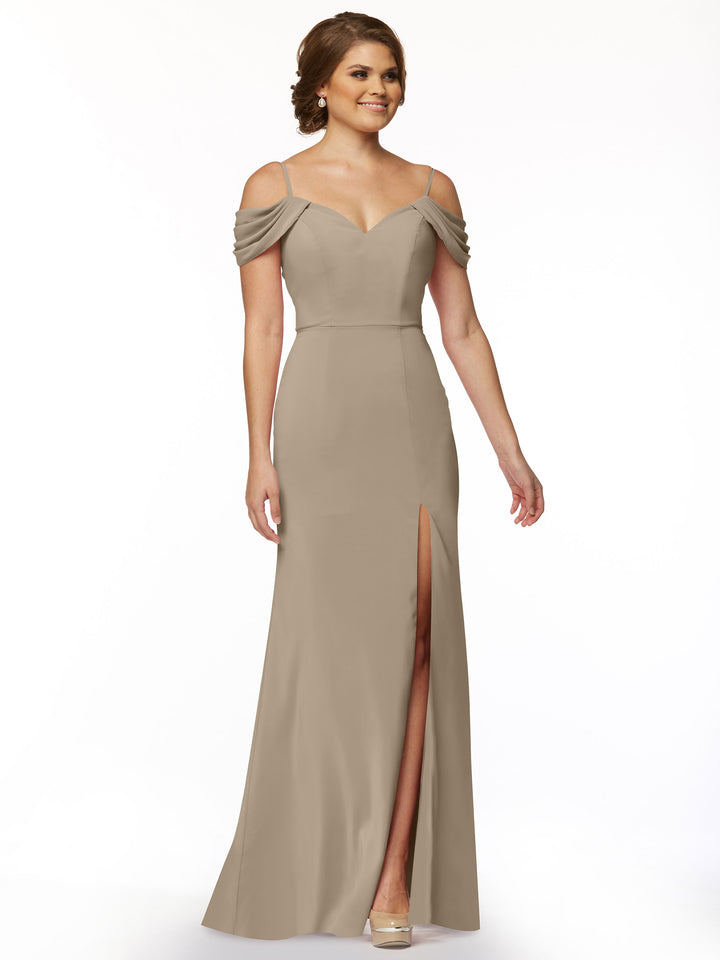 A woman models Avery Austin’s 83029: a taupe, floor-length off-the-shoulder dress with draped sleeves, fitted bodice, and thigh-high slit, standing against a plain white background.