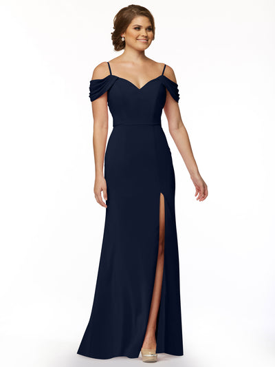 A woman smiles against a white background wearing Avery Austin style 83029, a navy off-the-shoulder dress with spaghetti straps, sweetheart neckline, draped sleeves, fitted bodice, and thigh-high slit.
