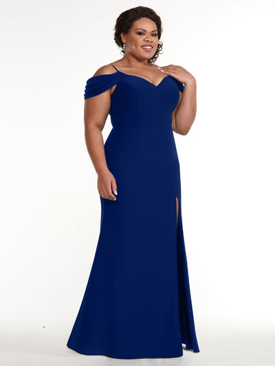 A woman smiles and touches her shoulder while wearing the Avery Austin 83029 fitted off-the-shoulder royal blue gown with a front slit, standing against a plain white background.