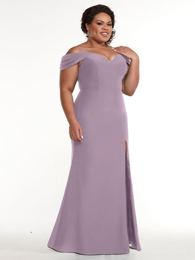 A woman wearing Avery Austin’s 83029, a lavender floor-length off-the-shoulder dress with a sweetheart neckline and thigh-high slit, stands smiling against a plain white background.